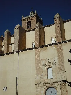 Vista de la fachada lateral de una iglesia con torre y detalles arquitectónicos del siglo XVI.