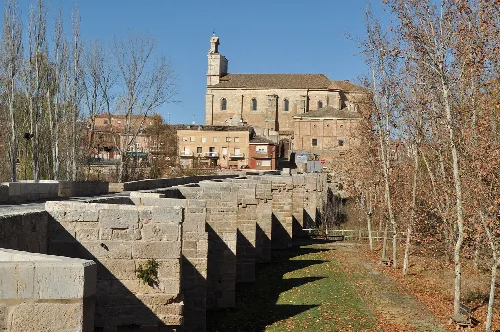 Stone bridge and church in Torquemada, Palencia, with leafless trees.