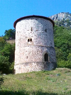 Runder Steinturm in Proaza mit kleinen Fenstern und rotem Ziegeldach.