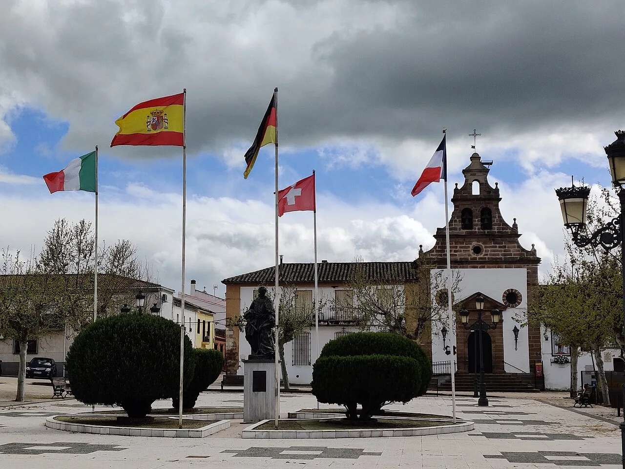 Flaggen auf dem Platz mit Kirche und Statue in Santa Elena, Jaén.