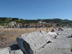 Felsen im Vordergrund und Strand mit Menschen und Gebäuden in Deva, Guipúzcoa.