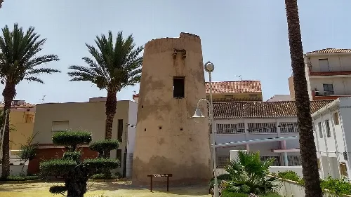 Wachturm mit Palmen und Gebäuden im Hintergrund.