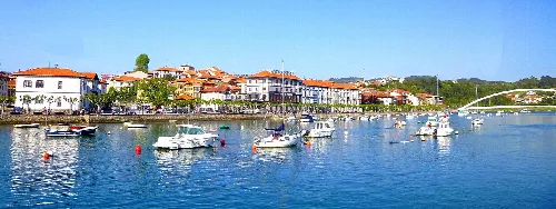 Barcos en la ría de Plencia con edificios y puente en el fondo.