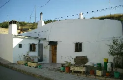 Weißes Haus in einer Höhle in Crevillente mit Pflanzen und Bänken draußen.
