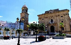 Square with church, clock, and trees in Chiclana de la Frontera.
