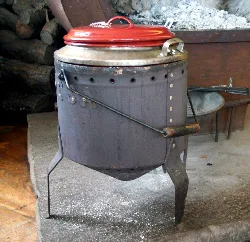 Old railway boiler with metal legs and red lid in a rustic setting.