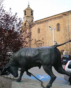 Estatua de un toro con soga en Lodosa, Navarra, frente a una iglesia antigua.