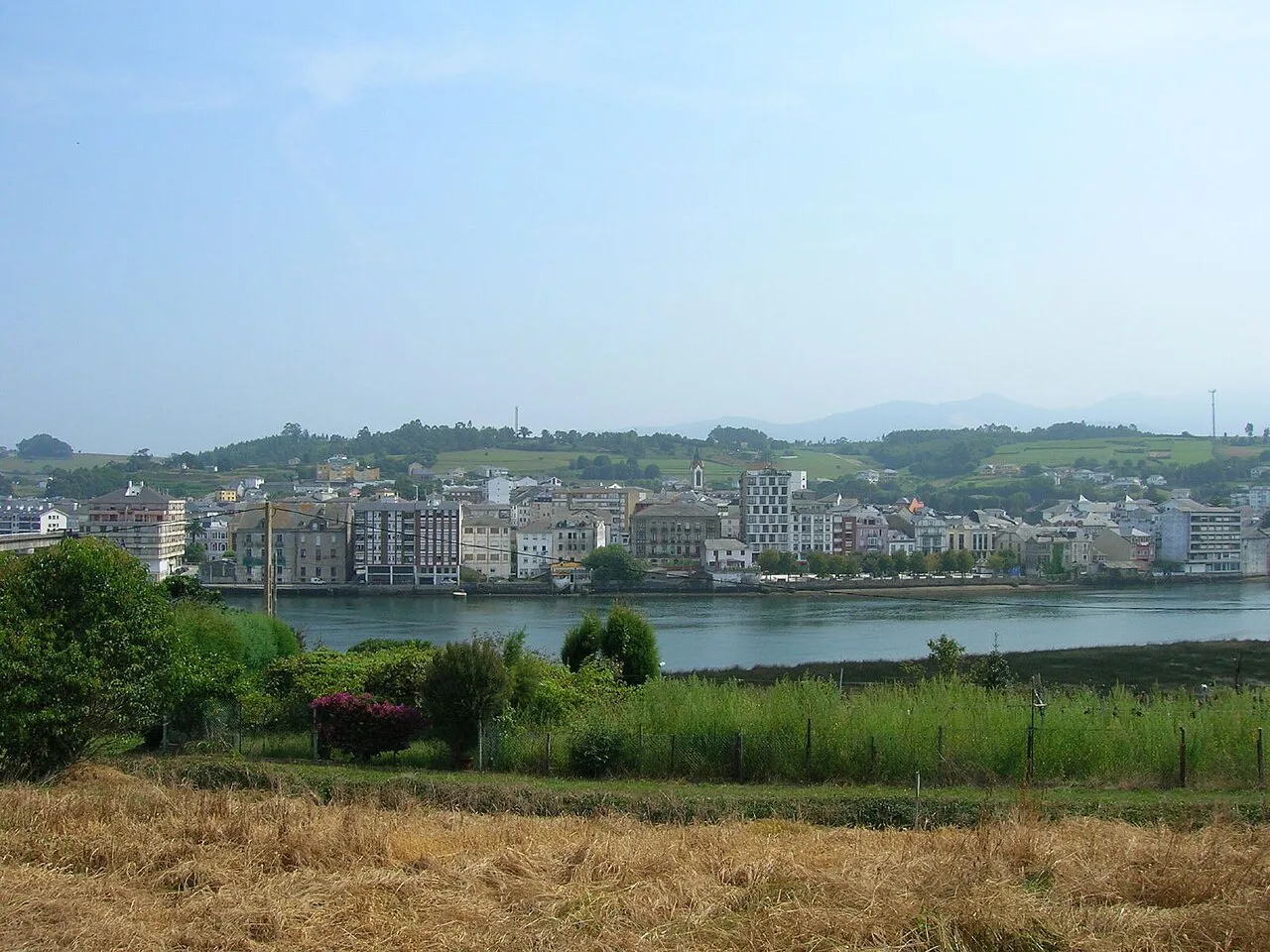 Vista de Navia con edificios y río, paisaje rural en primer plano.