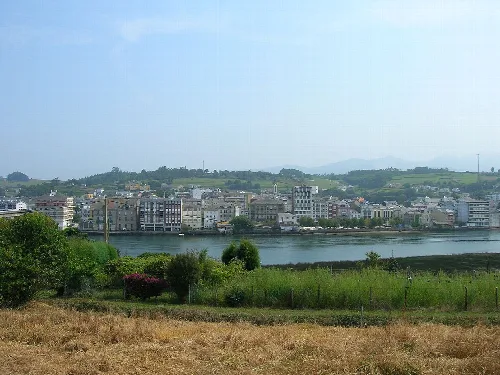 Vista de Navia con edificios y río, paisaje rural en primer plano.