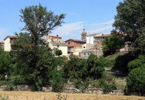 Häuser und eine Kirche in Tormantos, La Rioja, mit Bäumen und blauem Himmel.