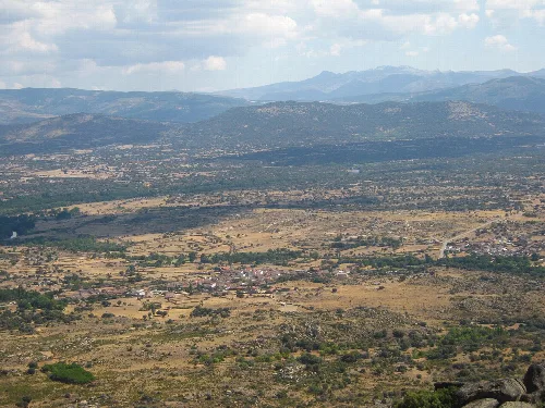 Weites Landschaftsbild mit Stadt, Feldern und Bergen im Hintergrund.