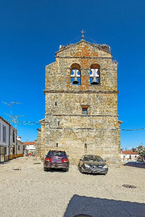 Stone bell tower with two bells and a cross on top.