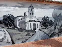 Mural de trampantojo en Alcolea de Tajo con iglesia y árboles en tonos grises.