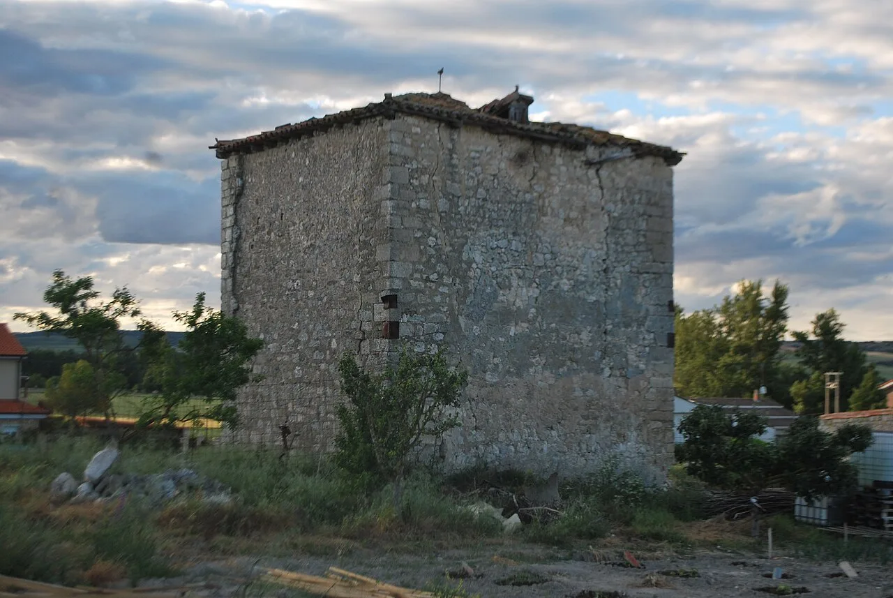 Stone tower with rectangular shape in a rural setting with vegetation and cloudy sky.
