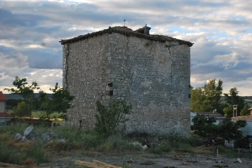 Stone tower with rectangular shape in a rural setting with vegetation and cloudy sky.