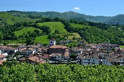 Blick auf eine Stadt mit Häusern und einer Kirche in einem Tal, umgeben von Bergen.
