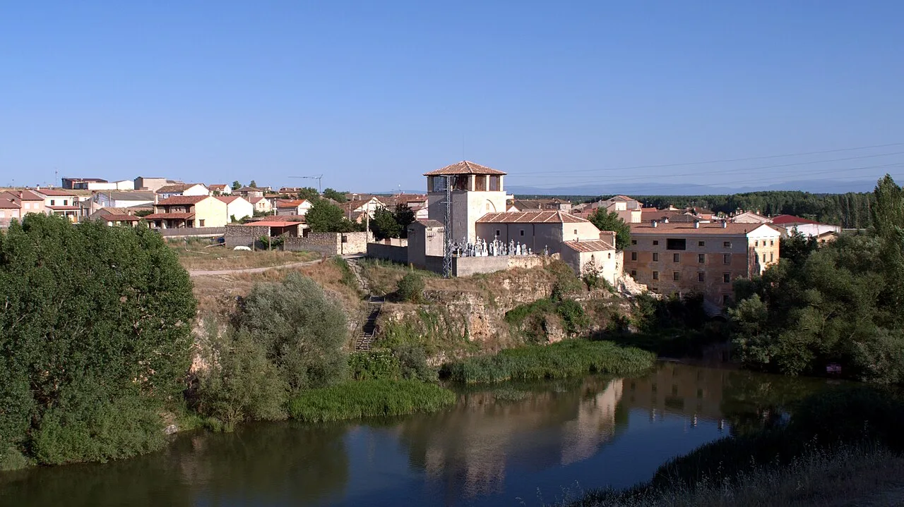 Vista del pueblo con iglesia y río en primer plano.
