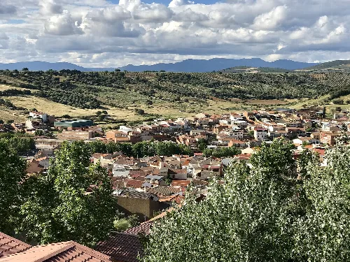 Blick auf eine Stadt mit roten und grünen Häusern in einem Tal, umgeben von Hügeln und Bergen.