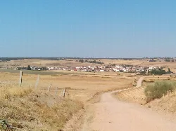 Schotterweg mit goldenen Feldern und einem Dorf im Hintergrund.