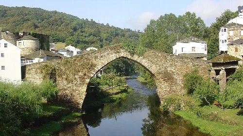 Steinbrücke über den Fluss in Navia de Suarna mit Häusern und Bäumen.