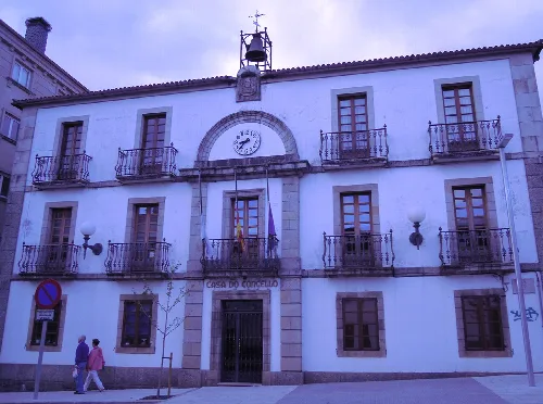 Fassade des Rathauses von Arzúa mit Uhr und Balkonen.
