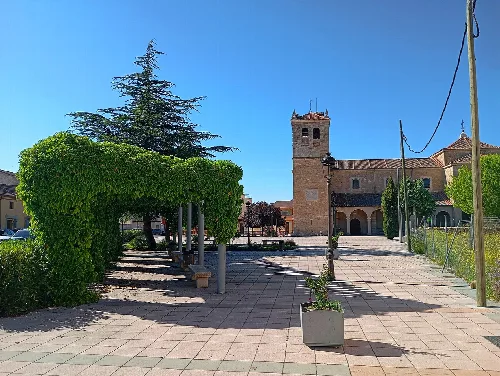 Square with trees, clock, and historic building in Abades, Segovia.