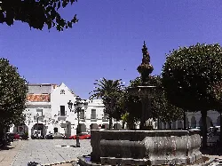 Fuente en la Plaza de España con árboles y edificios blancos.