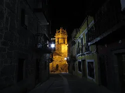 Narrow street with buildings and an illuminated church in the distance.