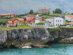 Llanes port lighthouse, colorful houses and castle in the background.