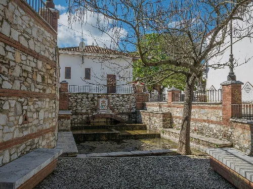 Brunnen mit Steinbänken und Baum in Fuenteheridos, Huelva.