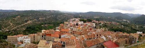 Vista panorámica de un pueblo con casas de tejado de teja y montañas al fondo.