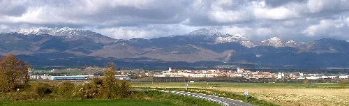 Landschaft mit Stadt und schneebedeckten Bergen im Hintergrund.