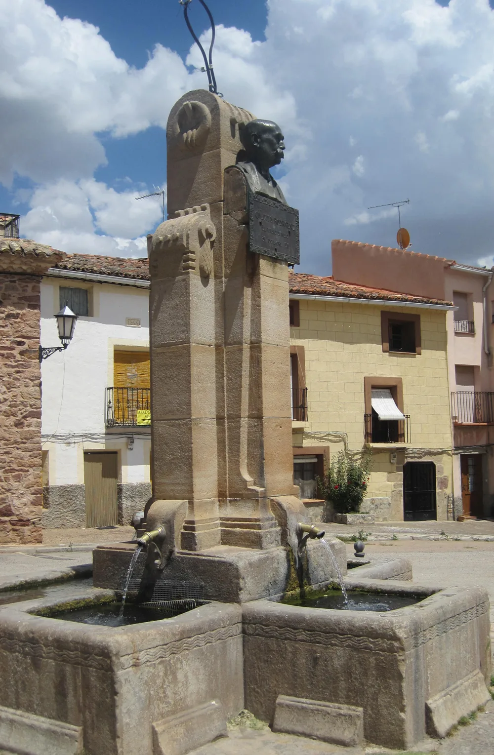 Stone fountain with a sculpture of a man on top and water flowing from two spouts.