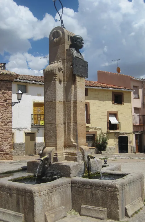 Steinbrunnen mit Skulptur eines Mannes oben und Wasser, das aus zwei Auslässen fließt.