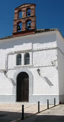 White facade with wooden door and red brick bell tower in Monturque.