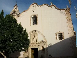 Fassade der Kirche Santa Maria la Major in Oliva mit architektonischen Details und einem Baum auf der linken Seite.