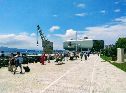 Seafront promenade with people, crane, and buildings in Santander.