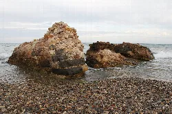 Restos de una torre de piedra en la playa con el mar y el cielo al fondo.
