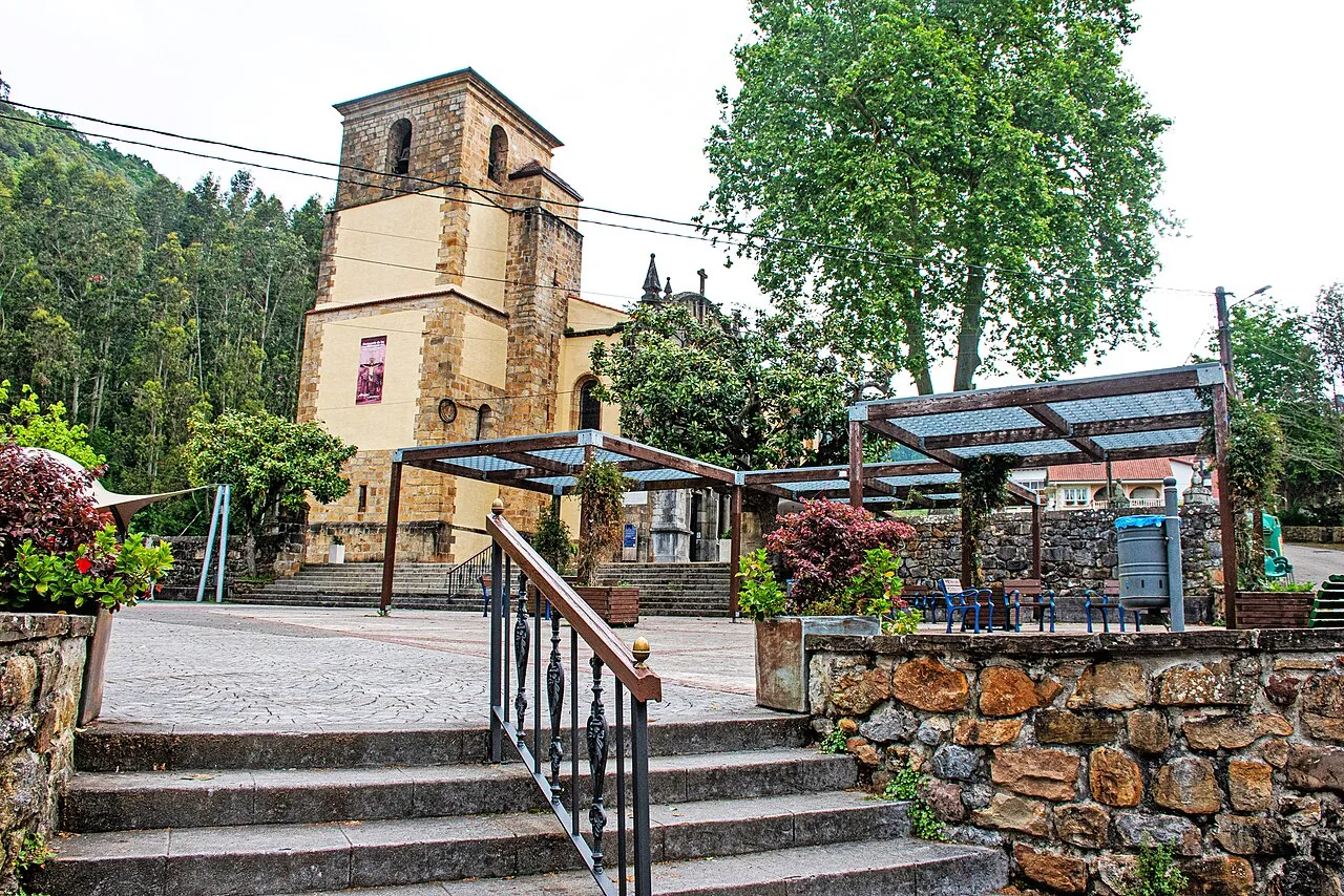 Platz in Limpias mit Kirche und Ruhebereichen, umgeben von Bäumen.