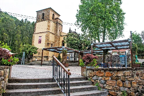 Platz in Limpias mit Kirche und Ruhebereichen, umgeben von Bäumen.