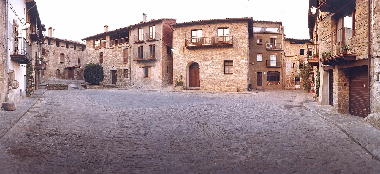 Fotografia de la Plaça del Gambeto de Riudaura i la façana de l'ajuntament del municipi al centre de la imatge.