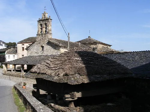 Vista del centro de San Martín de Oscos con un horreo de pizarra y paja y una iglesia antigua en el fondo.