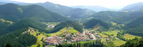Vista aérea de un pueblo en un valle rodeado de montañas y bosques.