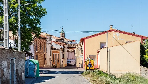 Street in Los Fayos with houses and a large tree on the left.