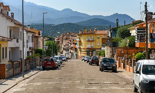 Straßenszene in Hostalric mit Häusern, Autos und Bergen.