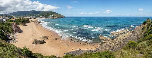 Vista panorámica de la playa de Baquio con arena, mar y colinas verdes.
