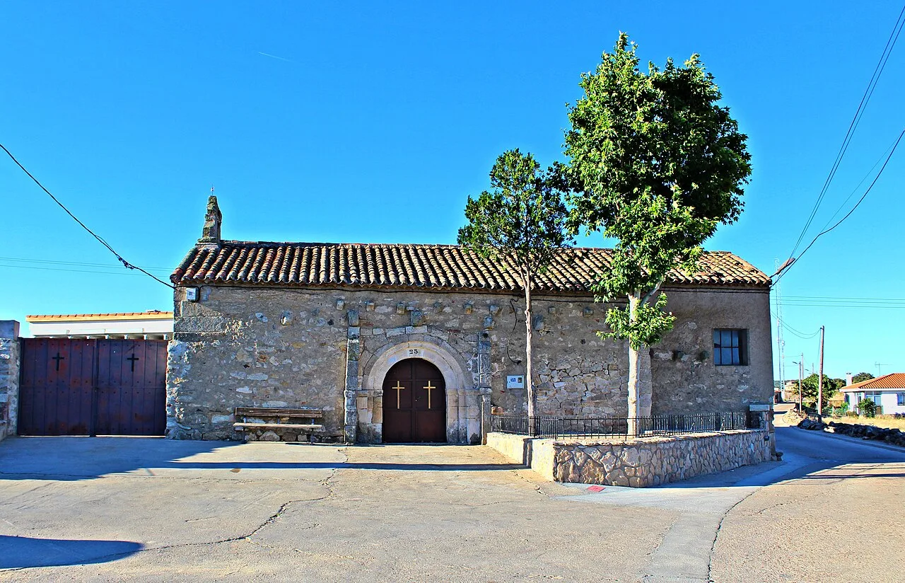 Stone church with wooden door and large tree in Zamayón.