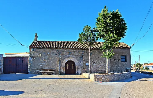 Stone church with wooden door and large tree in Zamayón.