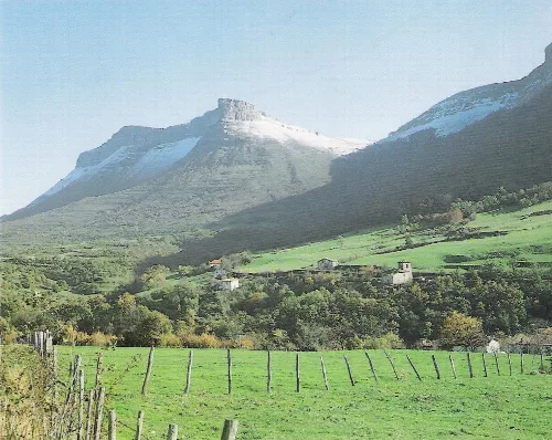 Mountains and houses in a valley with green fields.