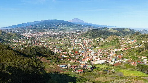 Landschaft mit Häusern, Bergen und Vulkan in der Ferne.